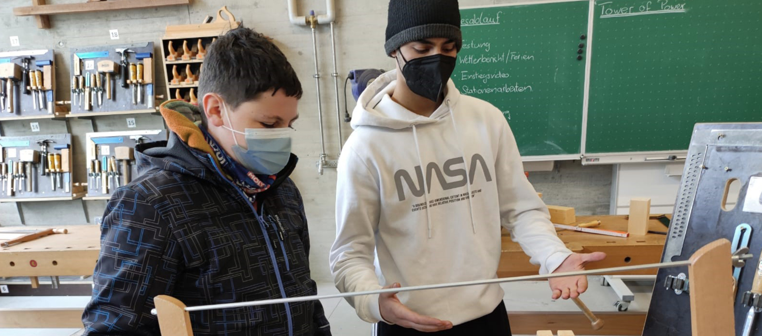 Zwei Schüler stehen in einem Werksraum. Sie arbeiten an einer Metall-Holz-Konstruktion.